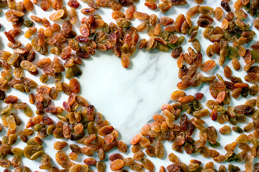 The raisins are located on a white surface in the shape of a heart. The concept is raw food, vegetarianism, healthy eating.