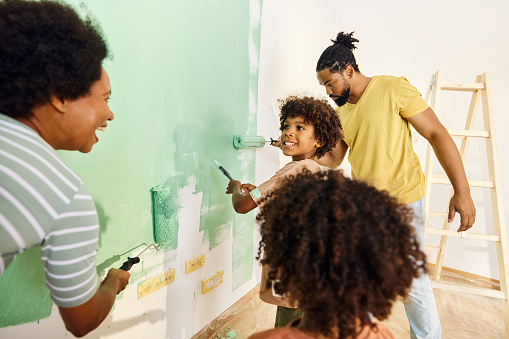 Black parents and their small kids cooperating while painting their walls during home renovation process.