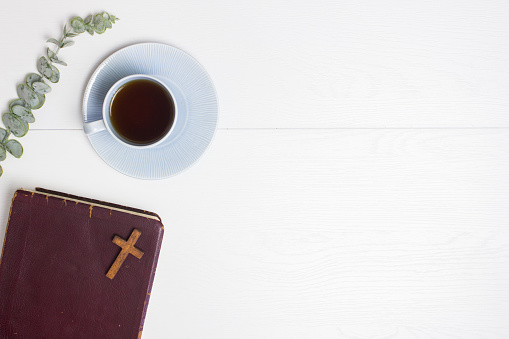Bible and coffee cup and green leaves over the white wooden background.