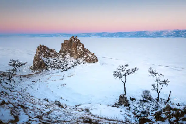 Frozen Baikal lake with snow in winter. Shamanka rock on Olkhon island at sunrise. Baikal, Siberia, Russia. Beautiful winter landscape