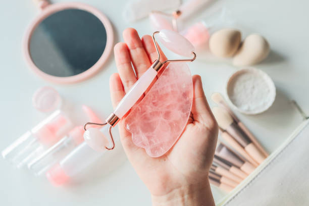 istock Woman holding gua sha tool and cosmetic over white table, top view 1430275040