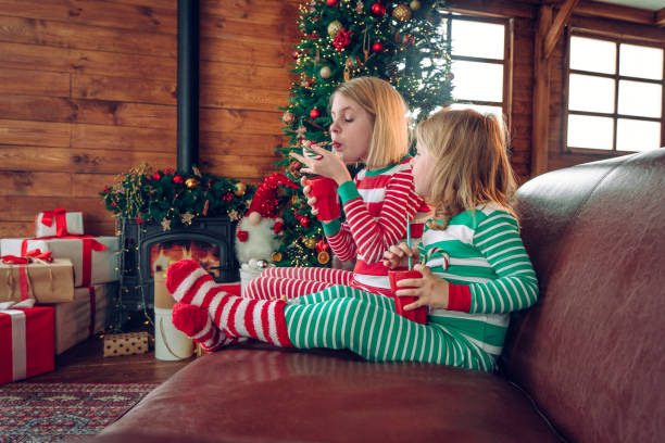 istock Two sisters drinking hot cocoa sitting near Christmas tree 1430277291