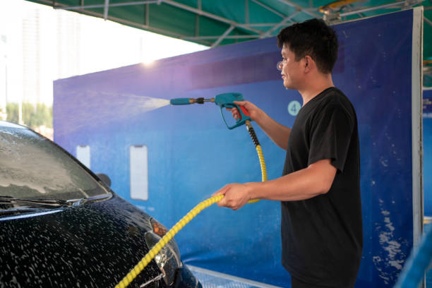 Man using high pressure water jet to wash car