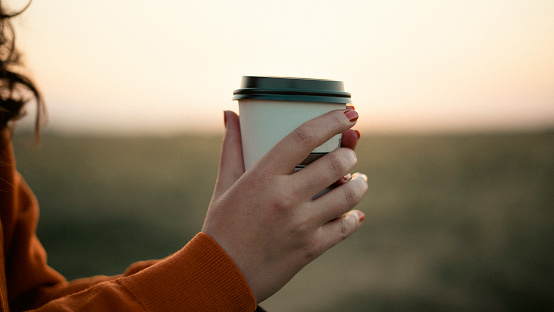 Woman holding mug of hot coffee at sunset