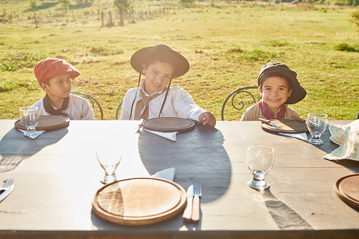 A waist up view of three gaucho boys sitting at a set table patiently waiting to be served lunch at the barbecue.
