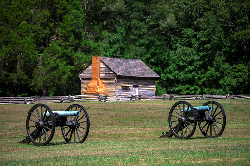 Front view of a blue M1857 12-Pounder, the Napoleon, an American civil war cannon at Shiloh National Military Park. With an old log cabin.