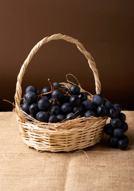 black Grapes in a basket on a black background and a mesh brown background