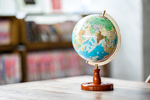 A miniature replica of the globe is placed on wooden table beside bookshelf in the library.
