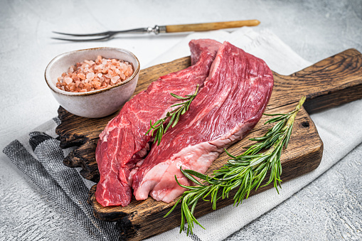 Butcher choise Bavette raw beef meat steak or flank flap on a wooden board with herbs. White background. Top view.