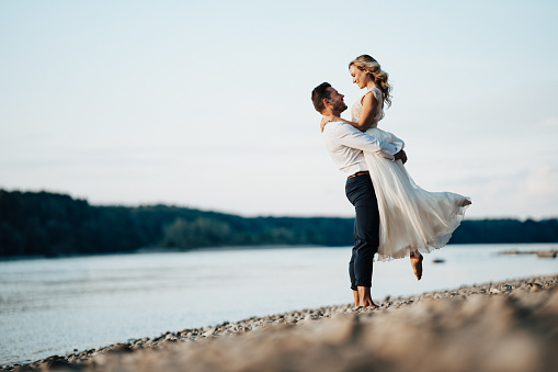 wedding day. beautiful bride in white long dress and young groom wearing in black suit are hugging in historic europe town.