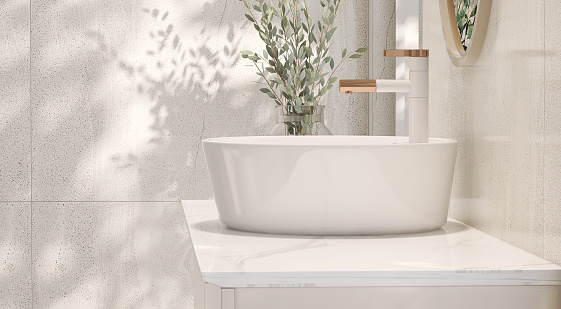 Diseño moderno y minimalista de tocador de baño de color crema con encimera de mármol y lavabo de cerámica redonda blanca con jarrón de plantas de interior a la luz del sol desde la ventana photo