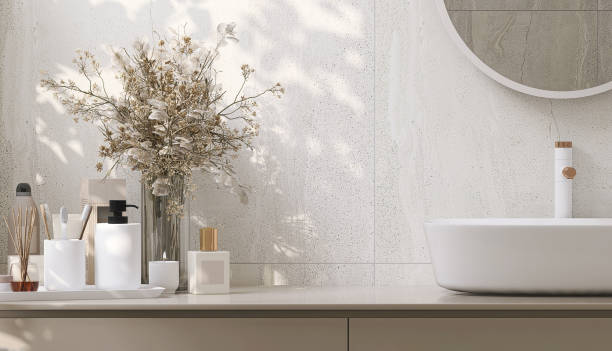 Modern and minimal design of beige colored bathroom vanity and white round ceramic washbasin with vase of houseplant in sunlight from window Modern and minimal design of beige colored bathroom vanity and white round ceramic washbasin with vase of houseplant in sunlight from window on granite tile wall for personal care and toiletries product display domestic bathroom stock pictures, royalty-free photos & images