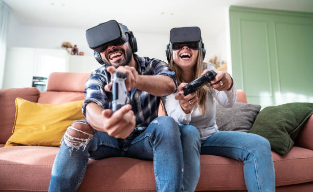 happy couple playing video games with virtual reality glasses - portrait of couple in vr glasses playing video game with joystick . virtual reality experience concept - gamer watching tv adult couple imagens e fotografias de stock