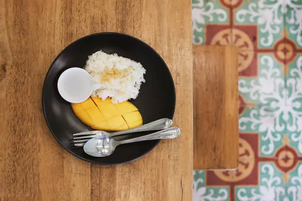 Fresh mango with sticky rice and sweetened coconut milk on wooden table. Popular Thai food prepared on plate to eat.