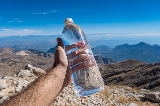 The model holds a 1 liter water bottle made of 1 pet 1 (1 pp). With gray cover. Clear sky blue. mountainous landscape,high altitude,nature scenery pov shot