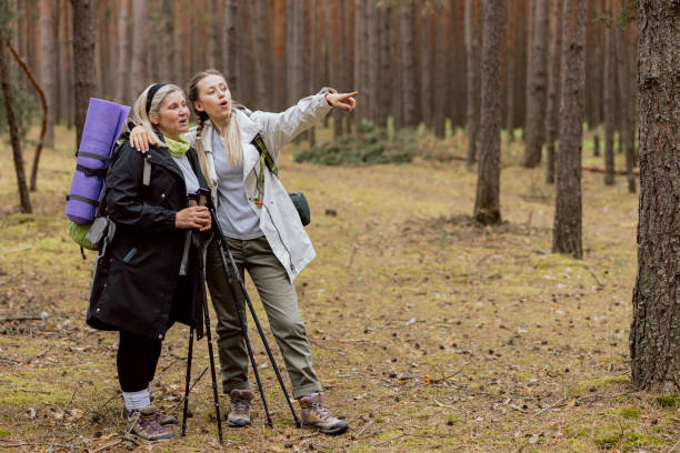 szczęśliwa mama i córka stojące w lesie po lewej stronie na zdjęciu. starsza kobieta trzymająca trecking equipmet buty wearinf kobiety przytulające się dyskutują patrząc na drogę - equipmet zdjęcia i obrazy z banku zdjęć