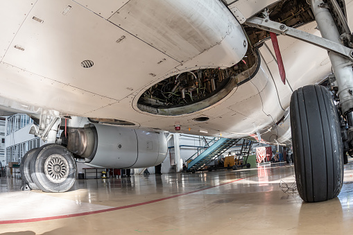 Close-up on the main landing gear of a white passenger aircraft and the bottom of the fuselage. The airplane is serviced in the hangar