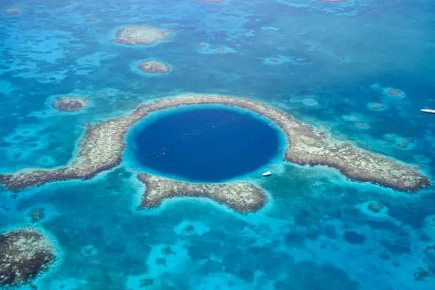 Aerial view of Great Blue Hole a marine sinkhole and geological wonder in the Belize Barrier Reef Reserve. A small white yacht is moored at it's edge