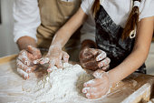 Close-up shot kid's hands and man's playing with flour on wooden surface. Sieving kneading process