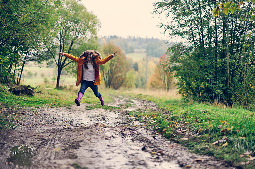 Happy teenage girl in galoshes jumping over autumn puddles.\nCanon R5