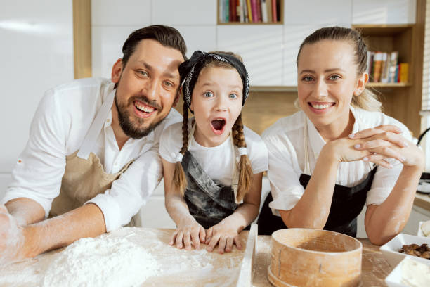 istock Curious daghter showing surprising emotions looking at camera. Happy father and mother looking laughing spending time together in modern kitchen at weekend 1430316974