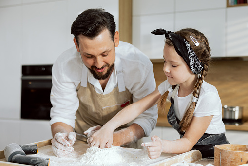 Curious daughter sieving flour on wooden surface with delighted young father. Preparing cooking pizza pasta cookies biscuits together.