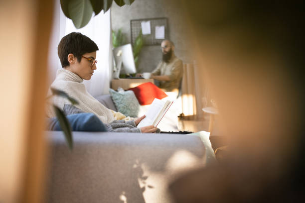 istock Young woman reading a book while her boyfriend is using a computer 1430317933