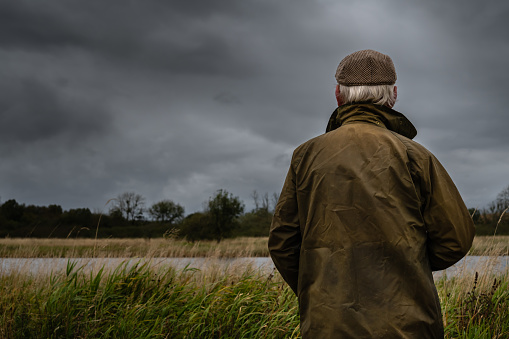 Rear view of a senior man looking at a river in a rural location in Scotland on an overcast morning