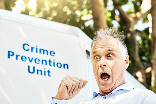 Mature man with an expression of comical fear and dismay as he stands beside a police sign.