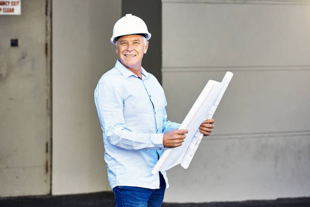 istock Middle-aged construction boss, civil engineer or architect wearing hard hat, smiles cheerfully as he holds plans outside a building 1430319665