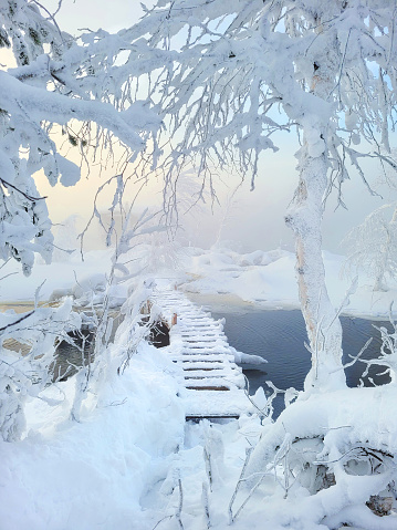 Winter snowy landscape with a wooden bridge on a small river, sunset