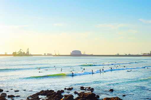 Surfers spot at Matosinhos beach, Leixoes port terminal building in background at susnet, Porto, Portugal