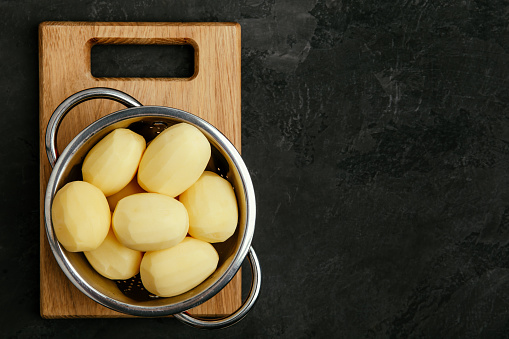 Potatoes. Fresh raw peeled potatoes in colander on dark stone background. Top view with copy space.
