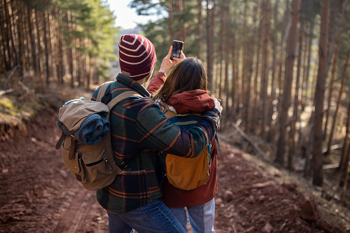 Young woman taking photos of nature using smart phone while hiking with her boyfriends on sunny day
