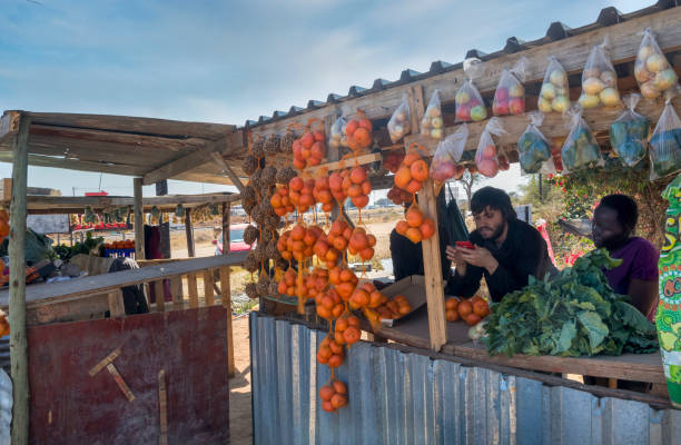 Caucasian man with a phone and African woman with a street stall with fruits and vegetables on display on the township