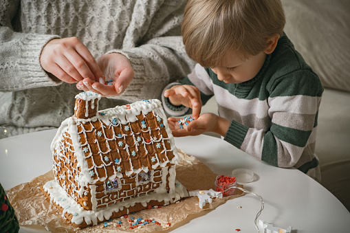 Stock photo showing elevated view of freshly prepared, homemade house-shaped gingerbread cookies decorated with white, glace icing forming a Christmas village themed party food idea.