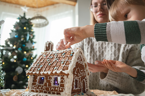 Child with mother decorating christmas gingerbread house together, family activities and traditions on Christmas and New Year's Eve