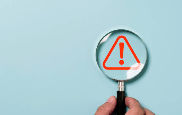 istock Hand holding magnifier glass with red triangle caution warning sign for focus notification error and maintenance concept. 1430347093