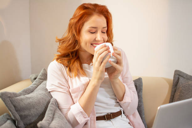 istock Beautiful smiling ginger woman smelling and drinking coffee while sitting on sofa at home. 1430351092