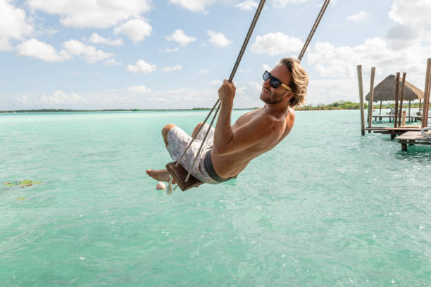 Young man having fun on swing in a beautiful lagoon on a sunny day