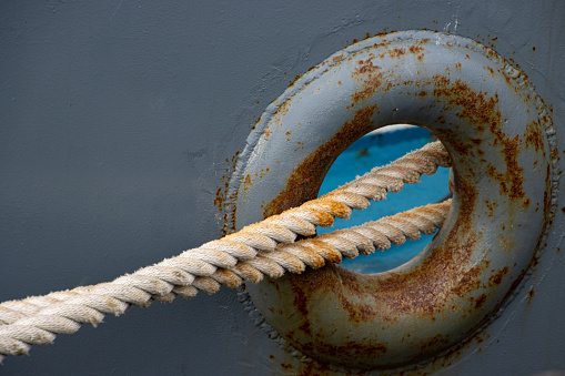 Close up of a mooring rope through a hole in a rusty boat