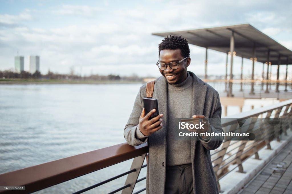 Afro american businessman using smart phone on city street Middle age Afro American businessman standing on street and using smart phone and bank credit card for online payment. Credit Card Stock Photo