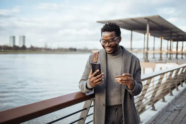 Photo of Afro american businessman using smart phone on city street