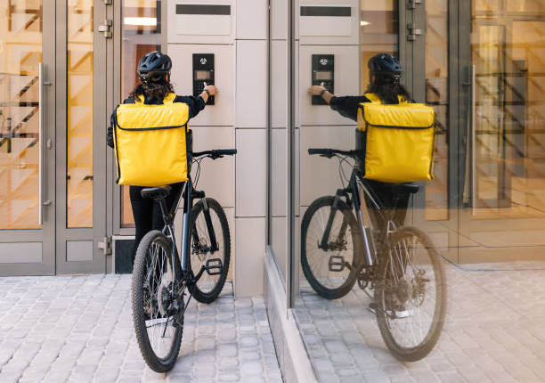 Rear view of a woman courier with backpack using an apartment intercom for delivery stock photo