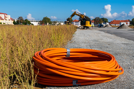 Roll of orange cable at construction site. Excavator in the background.