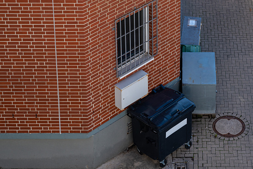 Black garbage container standing near the wall of the house. View from above.