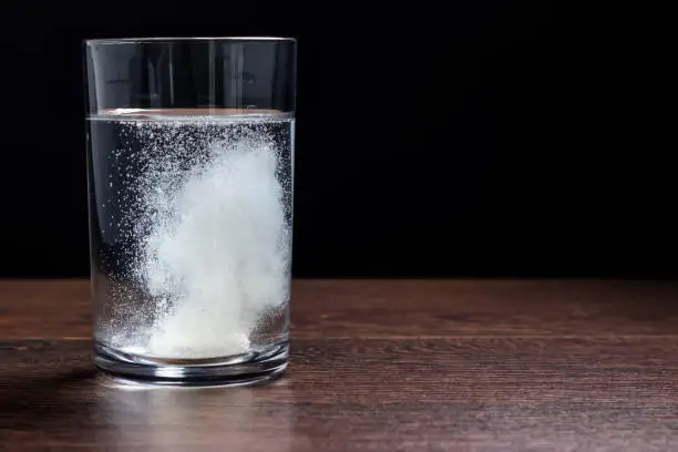 Effervescent tablet in a glass of water close-up on a black background. The concept of health