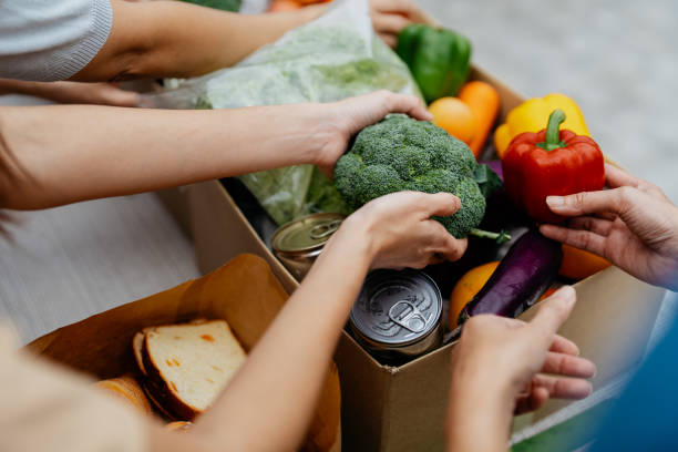 Asian volunteers packing donated goods and groceries at food bank Image of a group of asian volunteers packing donated goods and groceries to those impacted by financial difficulty. Asian volunteers setting up a charity food bank. donation box stock pictures, royalty-free photos & images