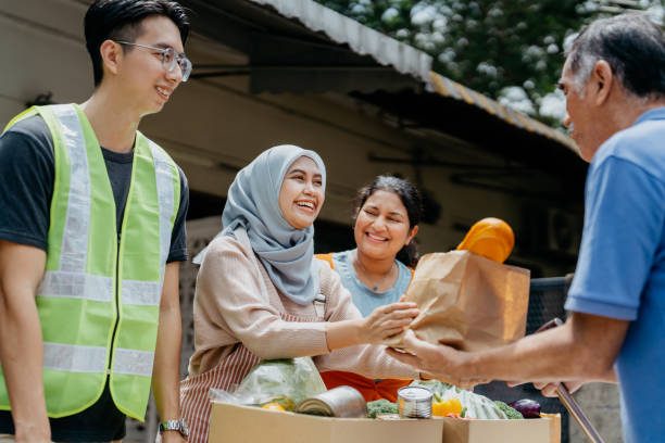 Female volunteers giving free food to elderly person at food bank Image of a group of multiracial Asian volunteers handing out free food to an elderly person at food bank community center food stock pictures, royalty-free photos & images