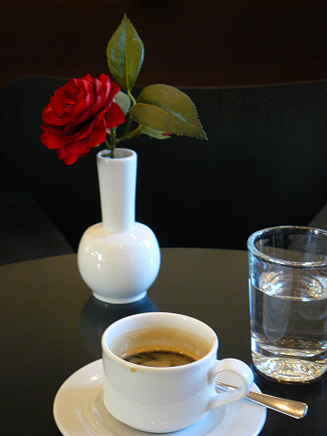 I saw the little still life in a café. The small vase with the red rose is the natural element. The glass of water and the espresso cup with the spoon form the opposite. The dark background and the black table are the contrast. Simplicity is the charm of the picture.